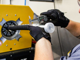 Technician measures a hydraulic hose fitting with digital calipers during assembly.