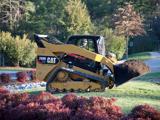 Compact track loader carries mulch through a landscaped area.