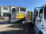 Portable air compressor supplies equipment at a residential construction site while workers prepare the property
