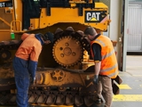 Two technicians inspect the undercarriage and tracks of a Caterpillar D6T dozer inside a service facility.